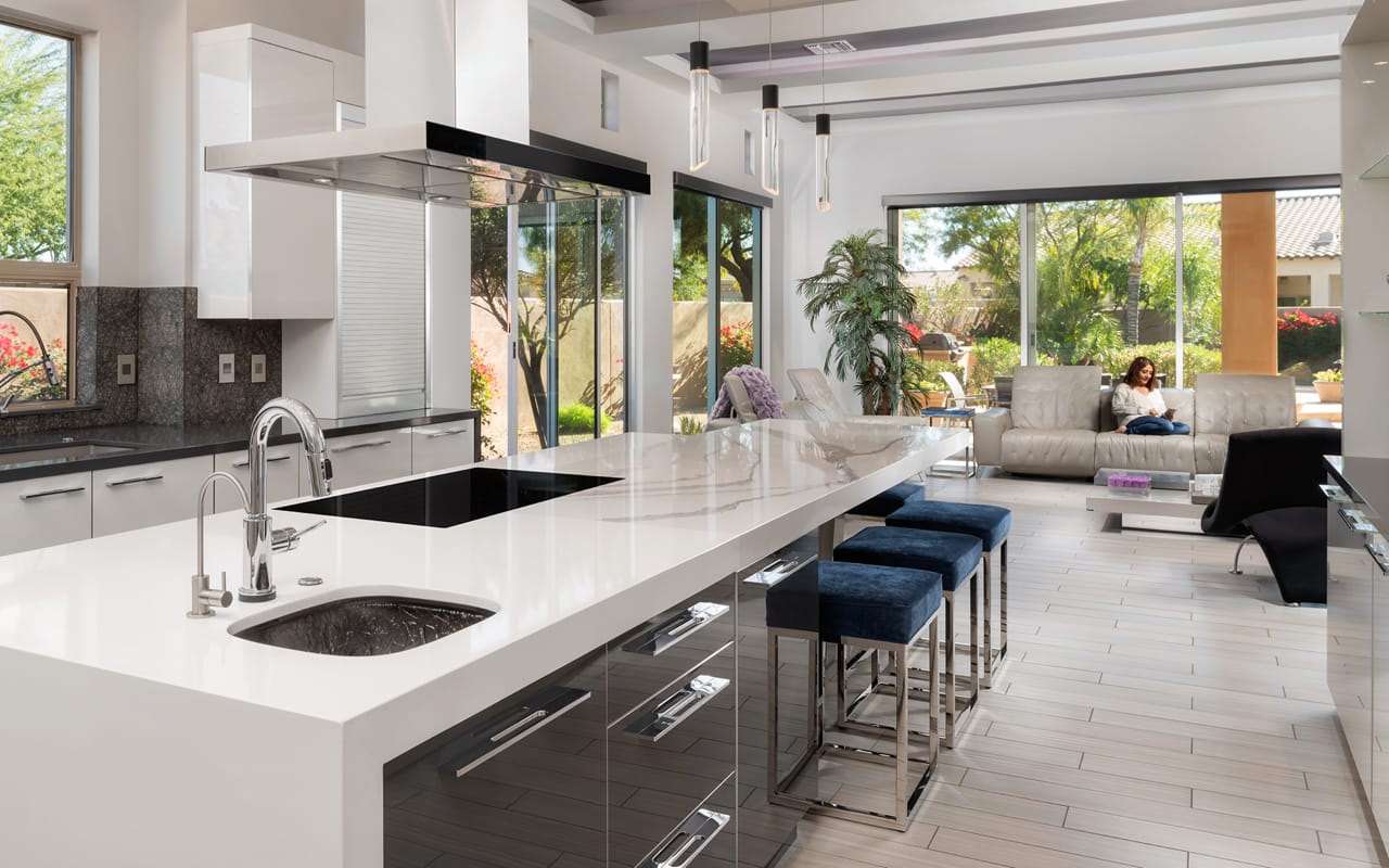 Contemporary white and grey Contemporary kitchen with a large kitchen island with seating. In the background there is a woman reading a book on the couch.
